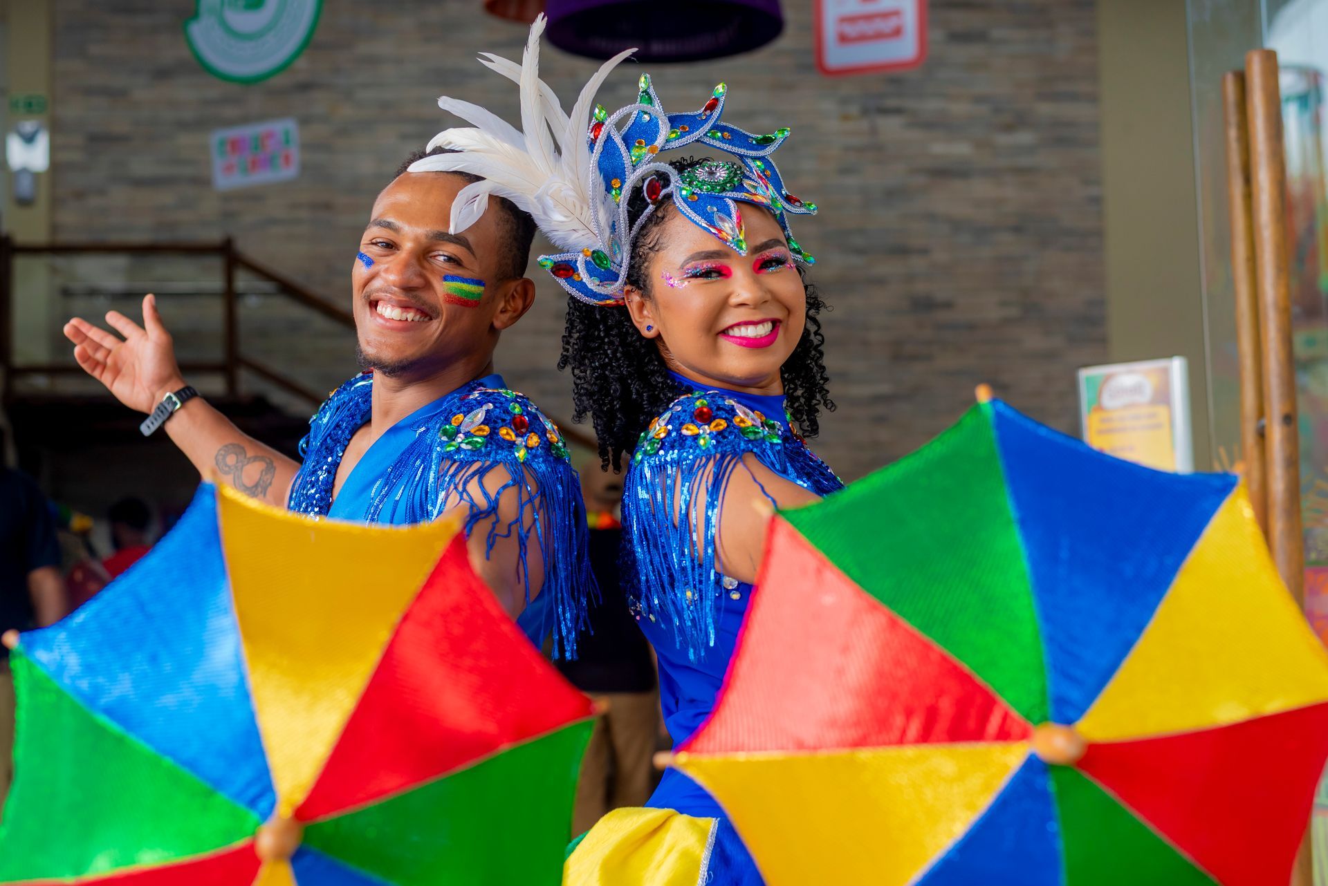 Um homem e uma mulher fantasiados de carnaval estão segurando guarda-chuvas coloridos.