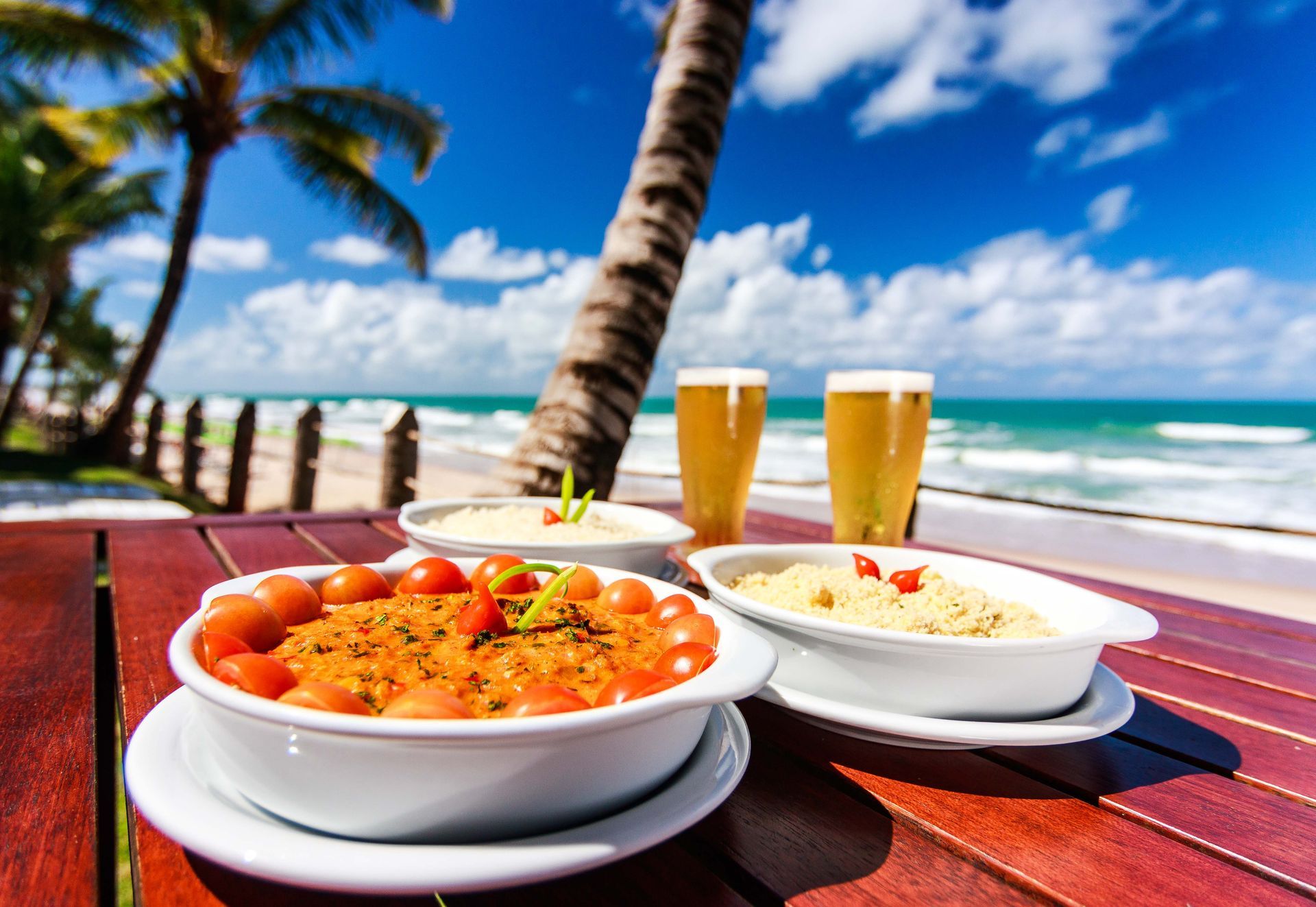 Uma mesa com tigelas de comida e dois copos de cerveja sobre ela.