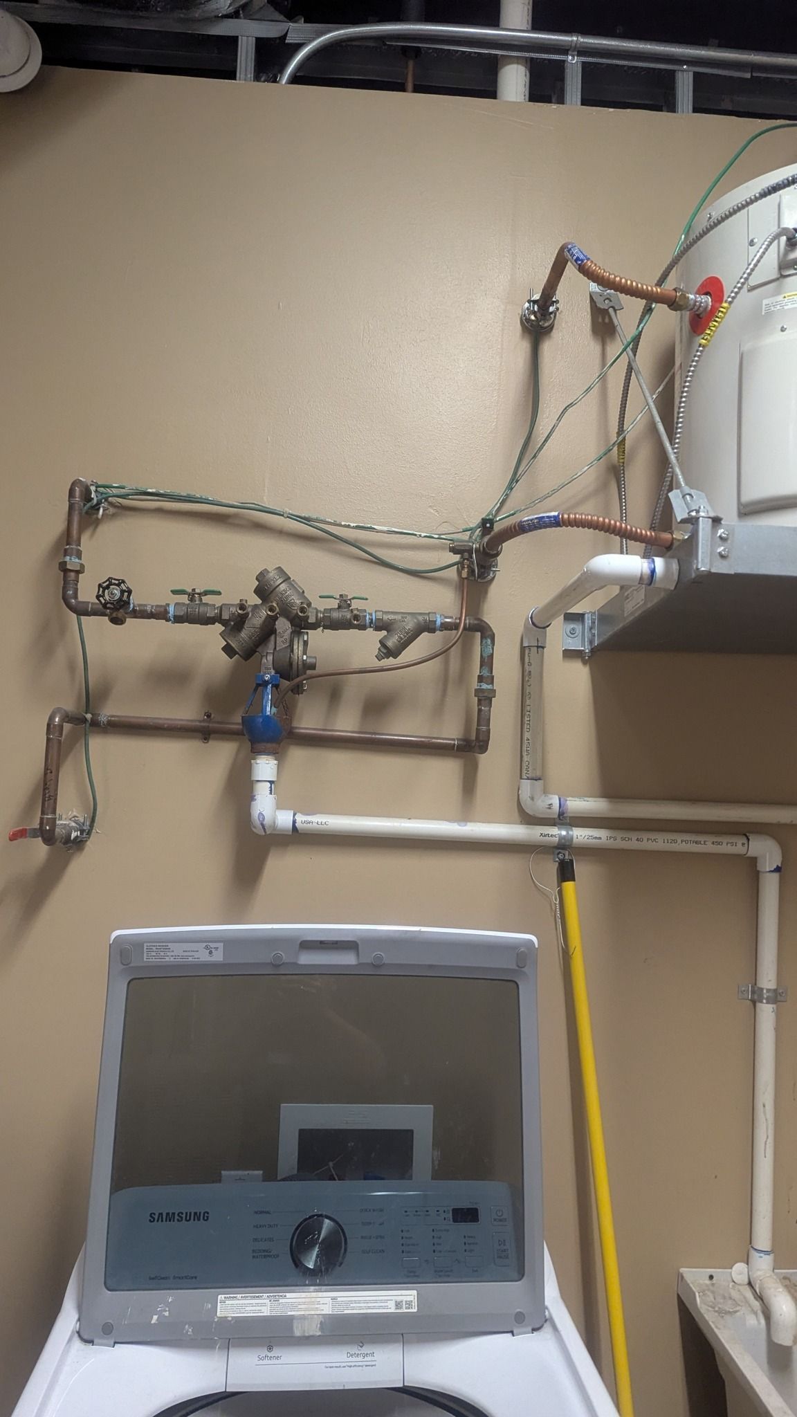Copper pipes and water heater on a wall above a washing machine.