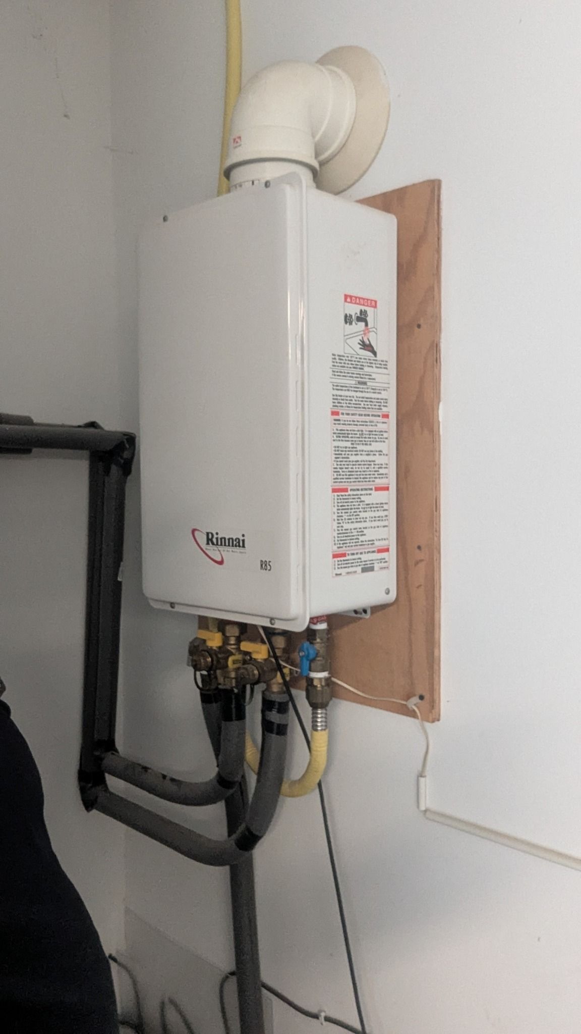White tankless water heater mounted on a wall with pipes connected.