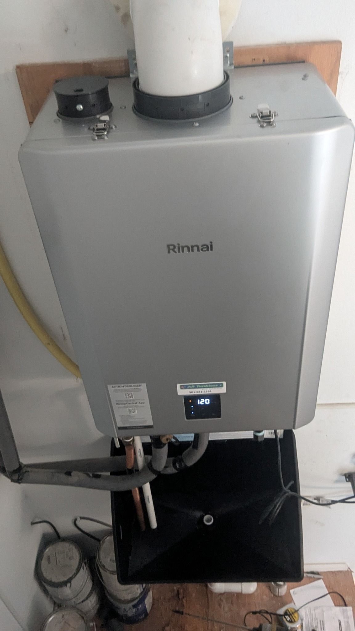 Rinnai tankless water heater mounted on a wall. Silver casing, white exhaust pipe, and digital display.