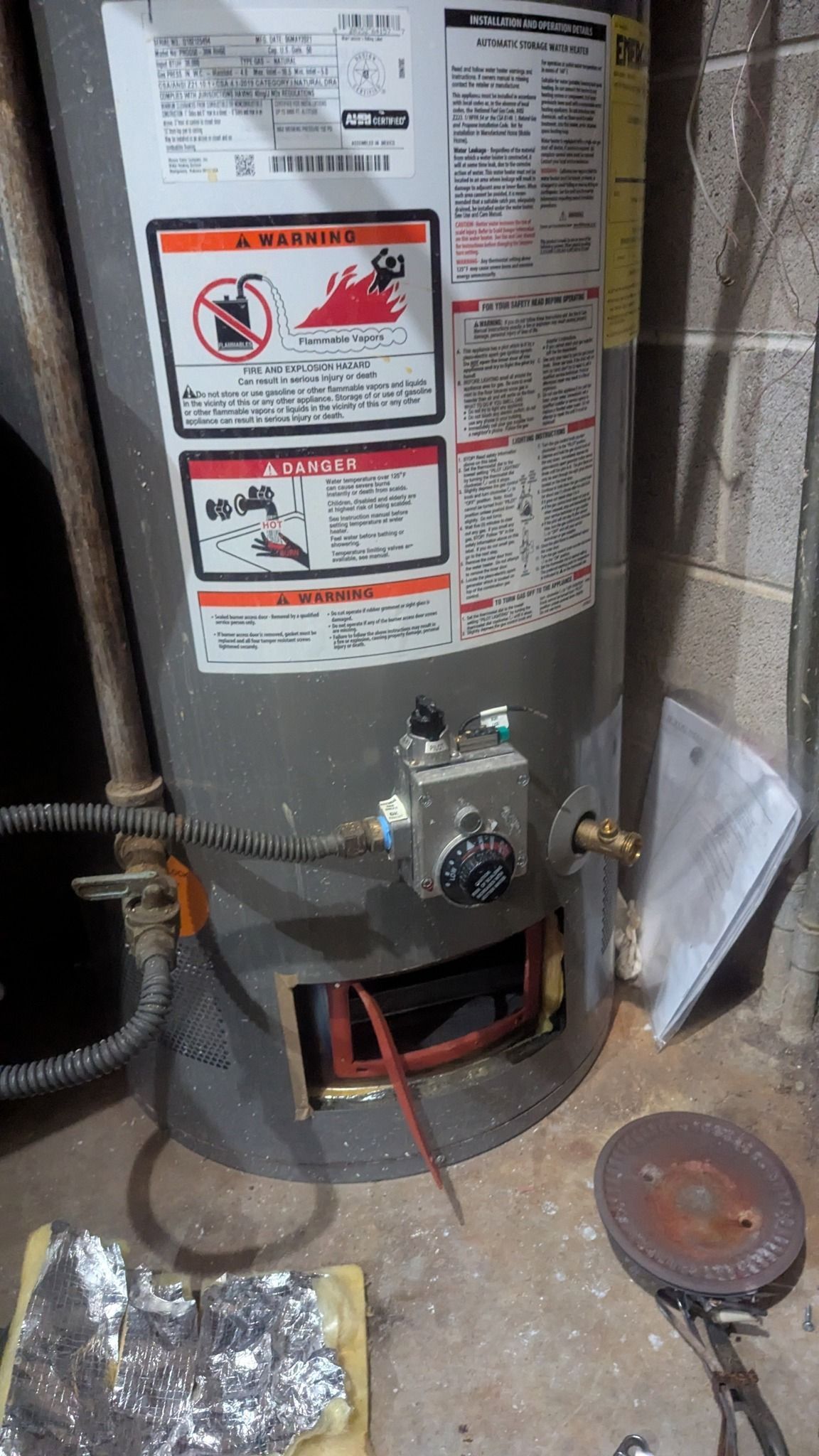 Gas water heater with open access panel, exposed wiring, and safety labels.