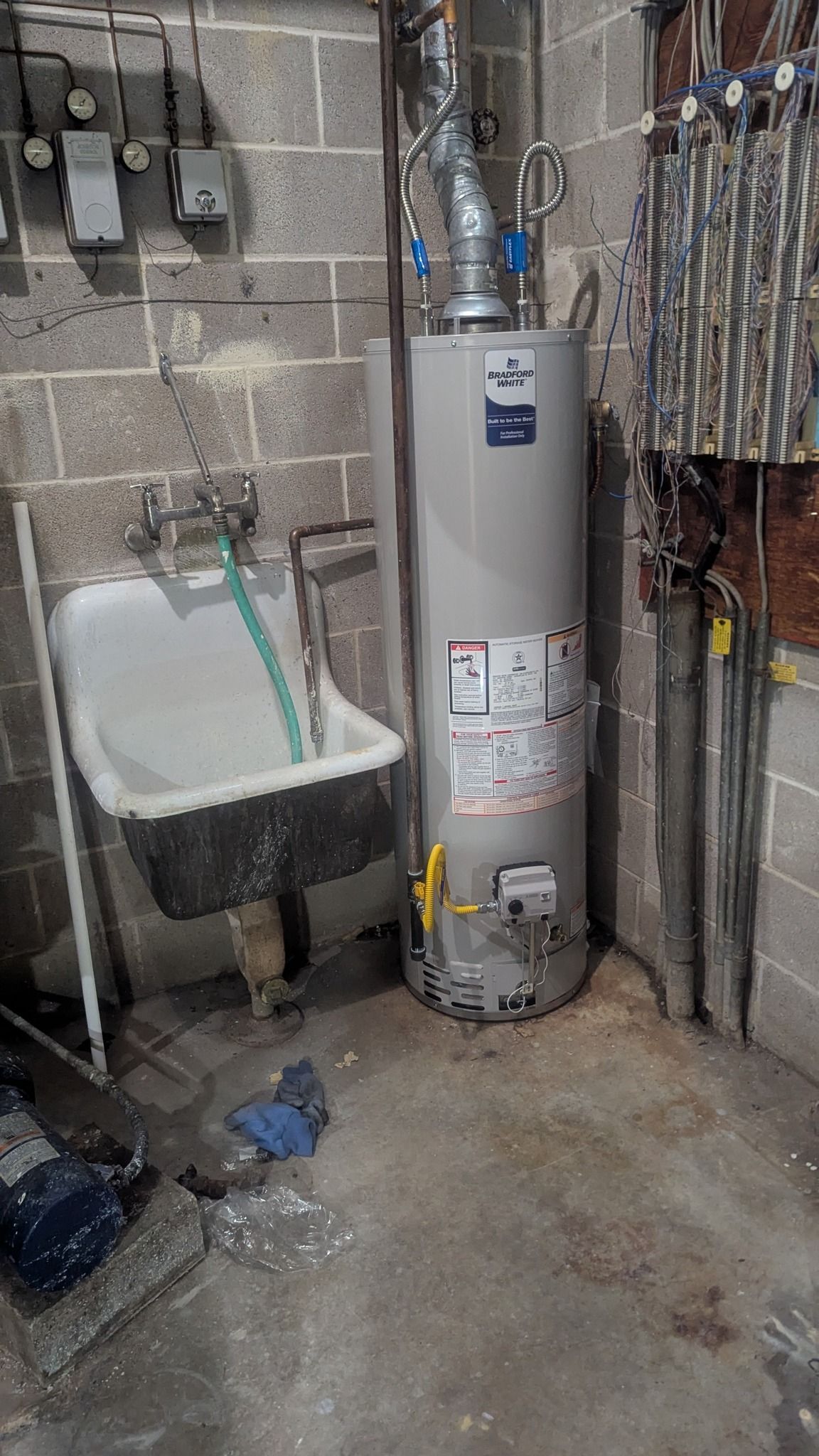 A water heater next to a utility sink in a concrete basement.