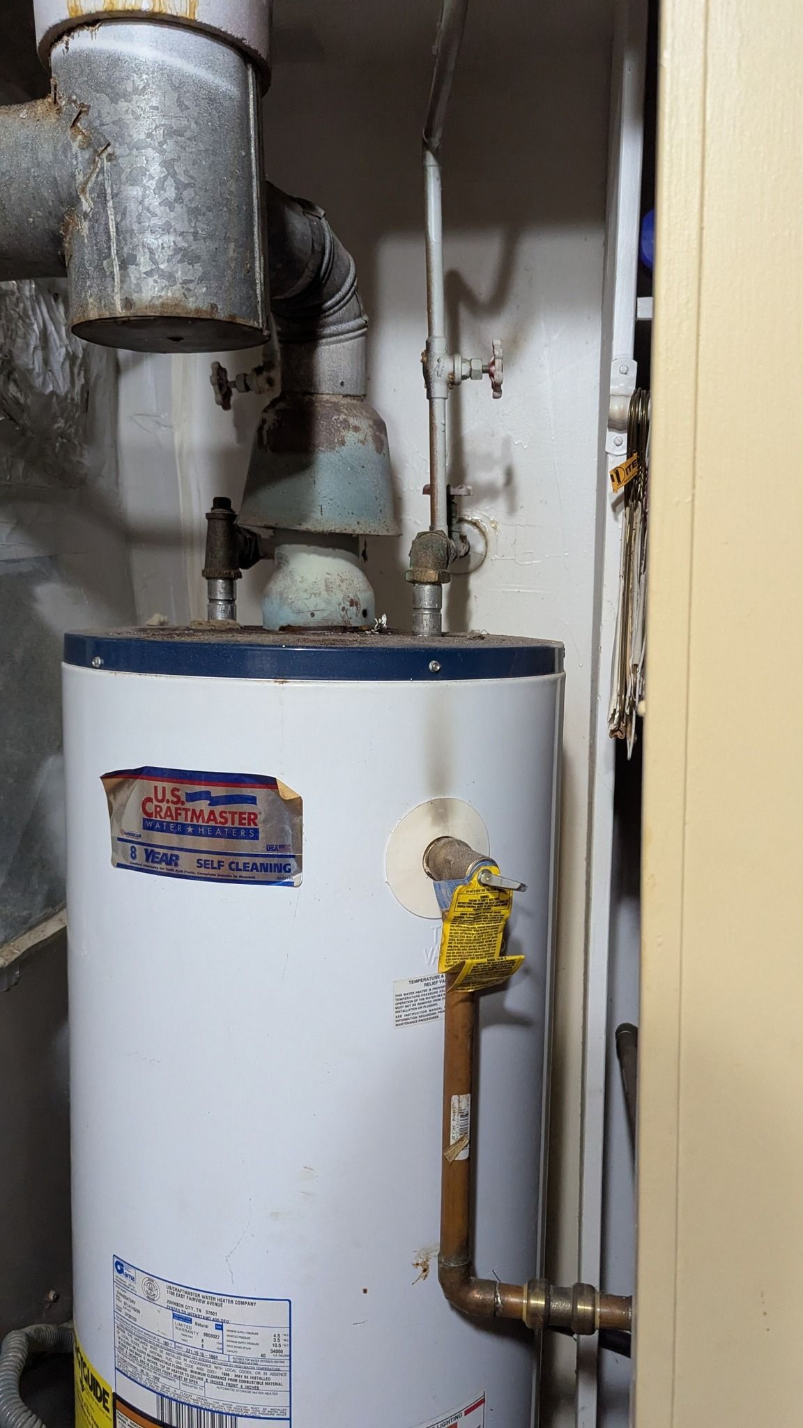 White water heater with rusted exhaust pipes in a utility room.