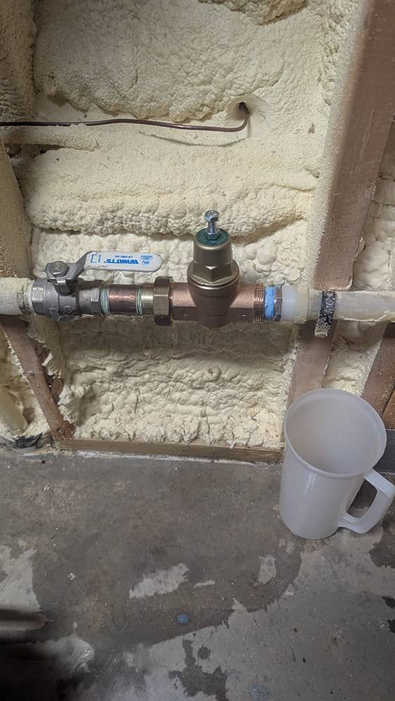 Water pressure regulator valve with copper piping and a white mug in a basement.