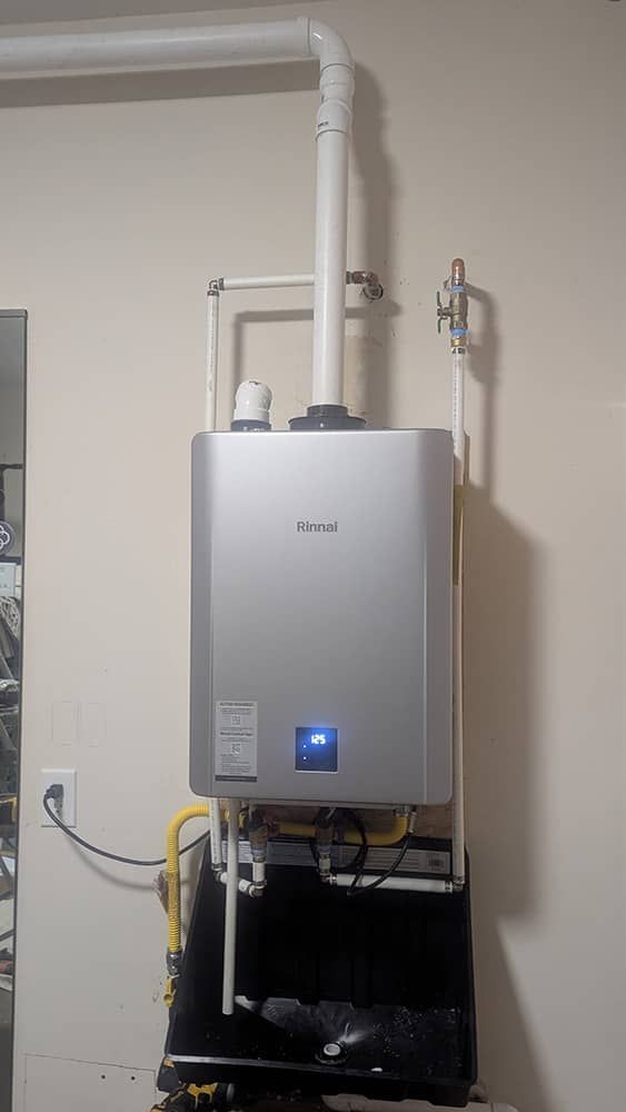 Tankless water heater installed on a wall with venting and gas lines, inside a garage.