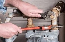 A person using wrenches to work on pipes outdoors, likely a repair or installation.
