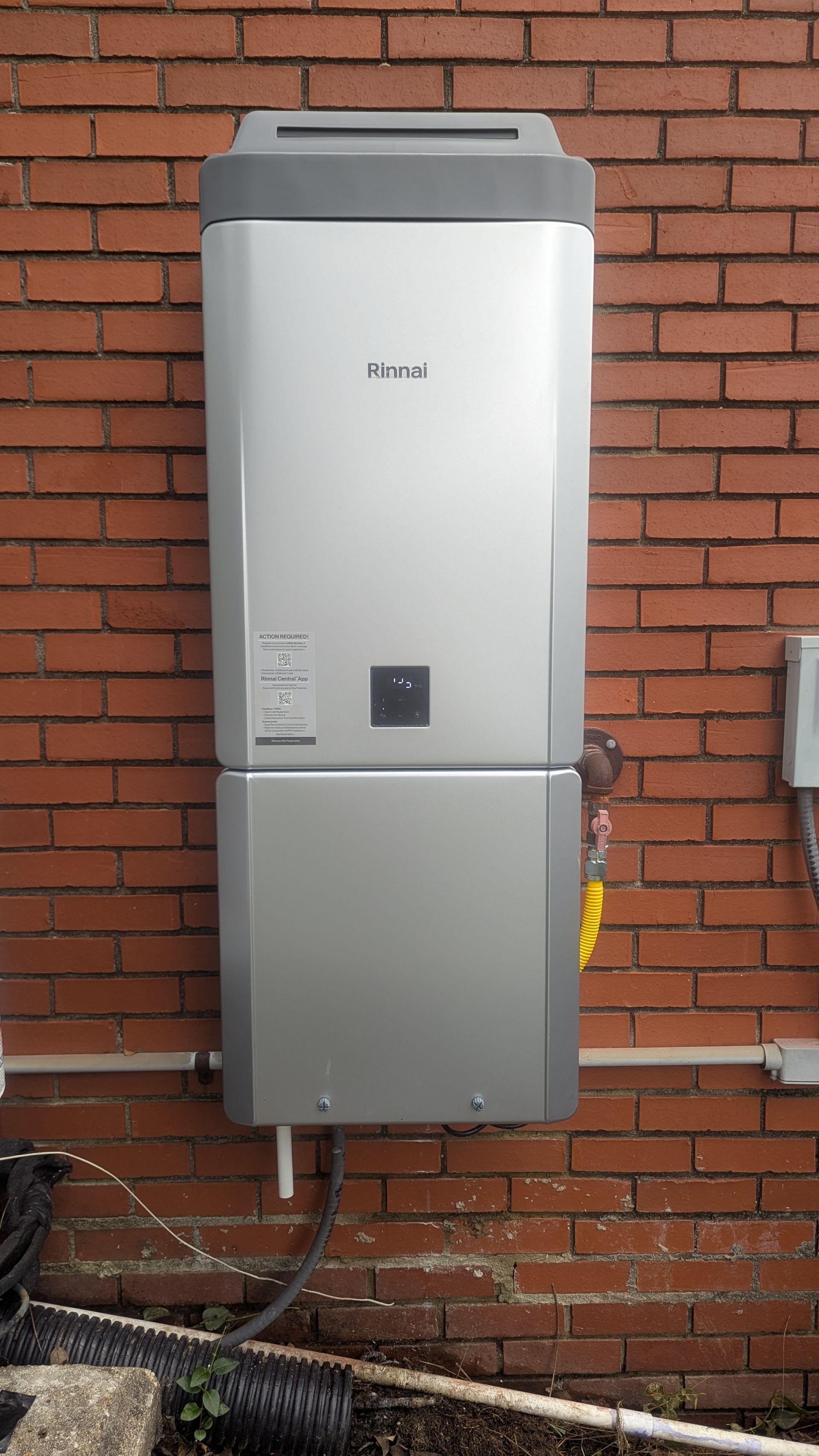 Silver solar battery on a red brick wall; a white pipe and black wires are below.