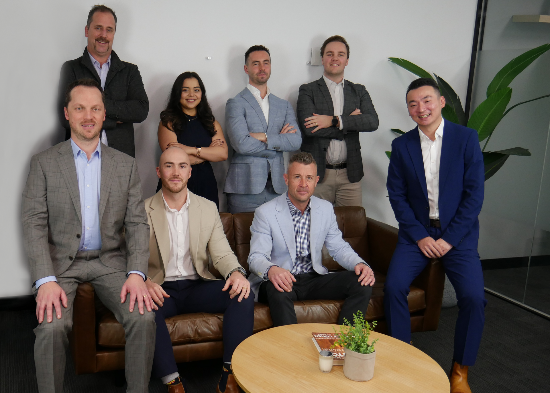 Group of nine professionals, diverse in appearance, in business attire, posing for a photo in an office setting.