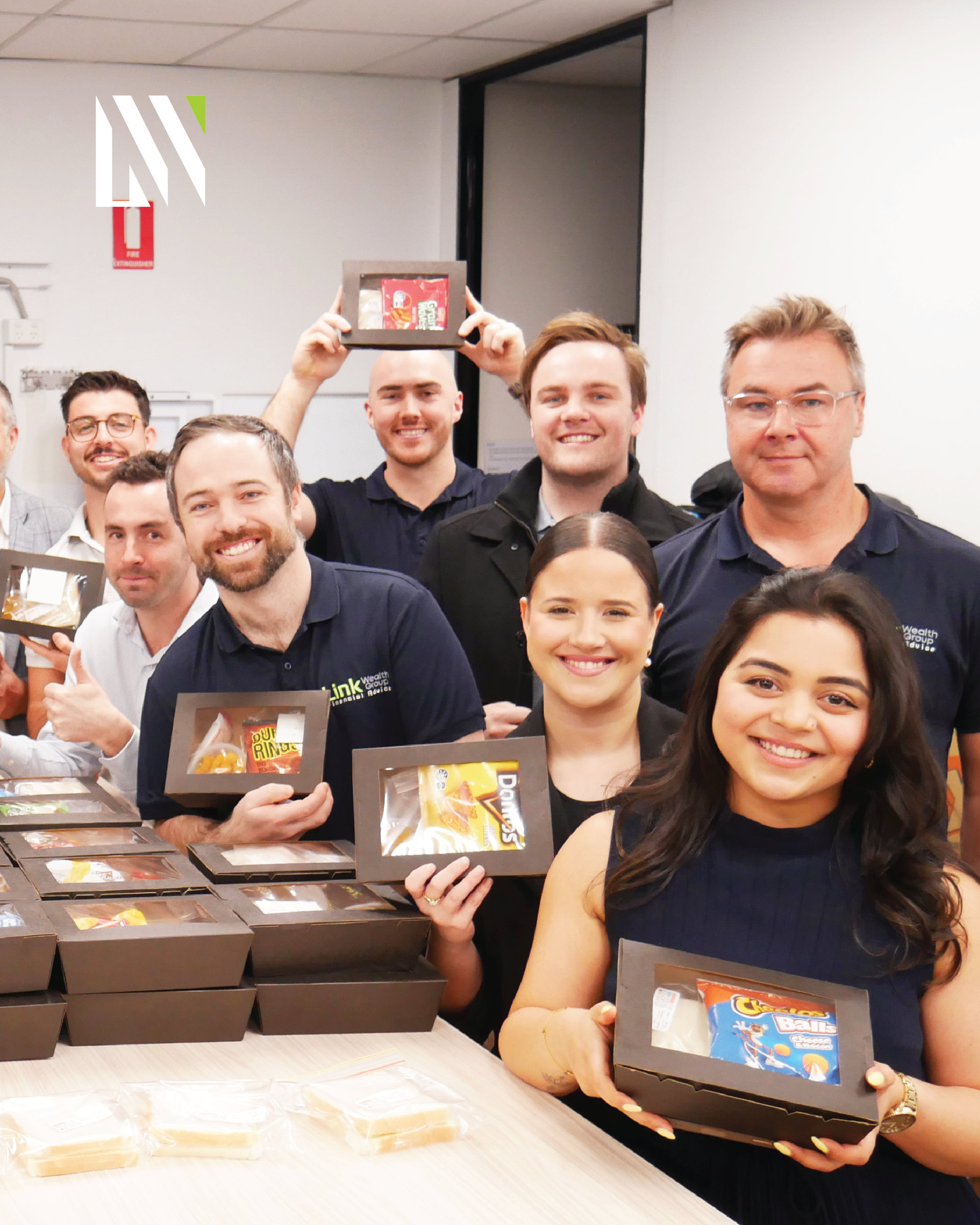 Group of people smiling and holding food boxes in an office.