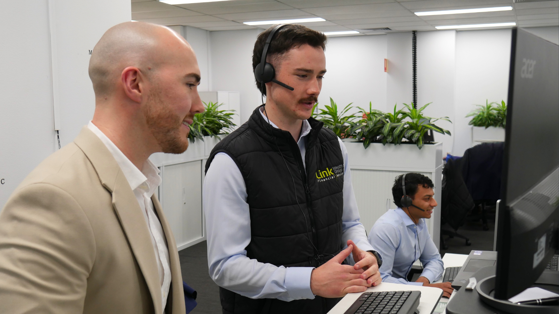 Two men smile at the camera in an office setting. One wears a blue shirt; the other, a sweater.