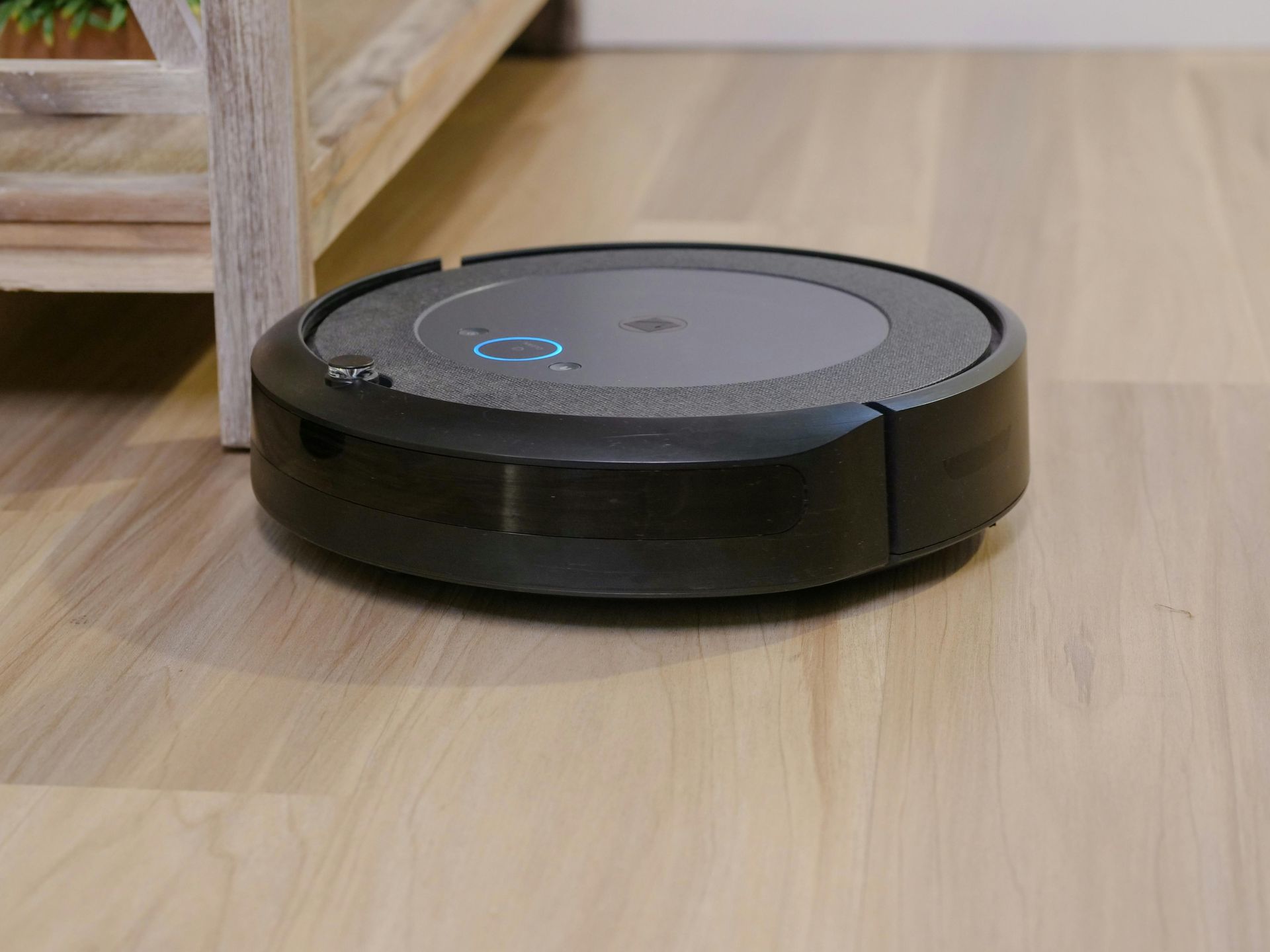 A smart black robot vacuum cleaner is sitting on a wooden floor.