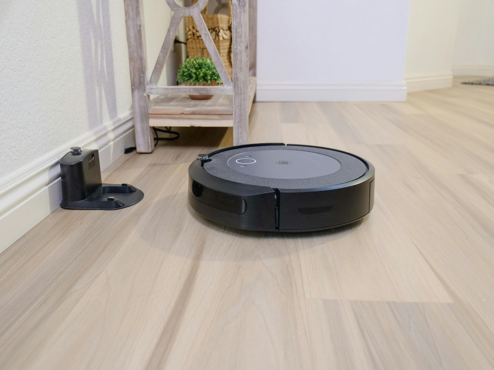 A smart robot vacuum cleaner is sitting on a wooden floor next to a charging station.