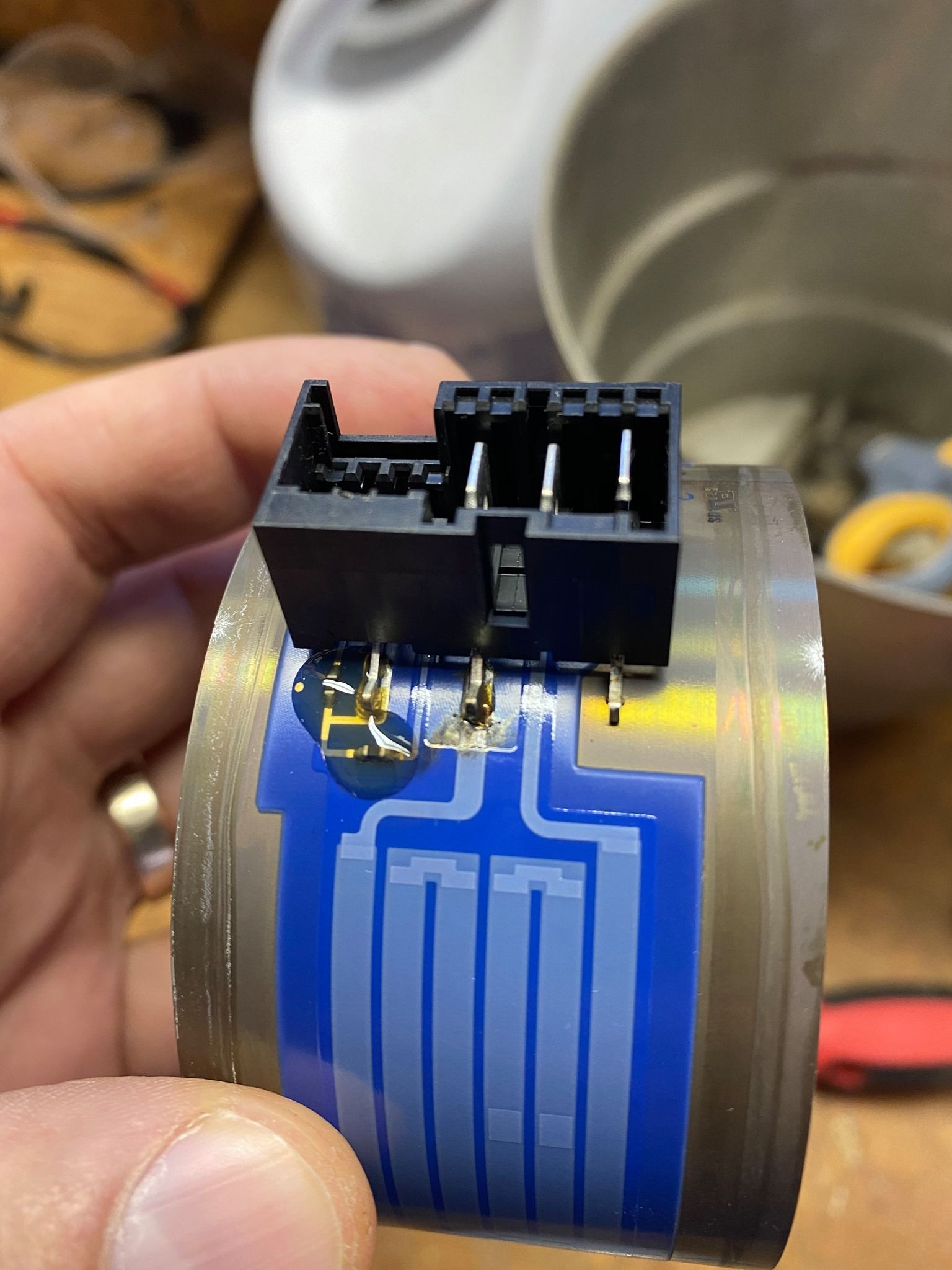 A hand holding a metal cylinder with blue, circuit-like design and a black electrical connector.