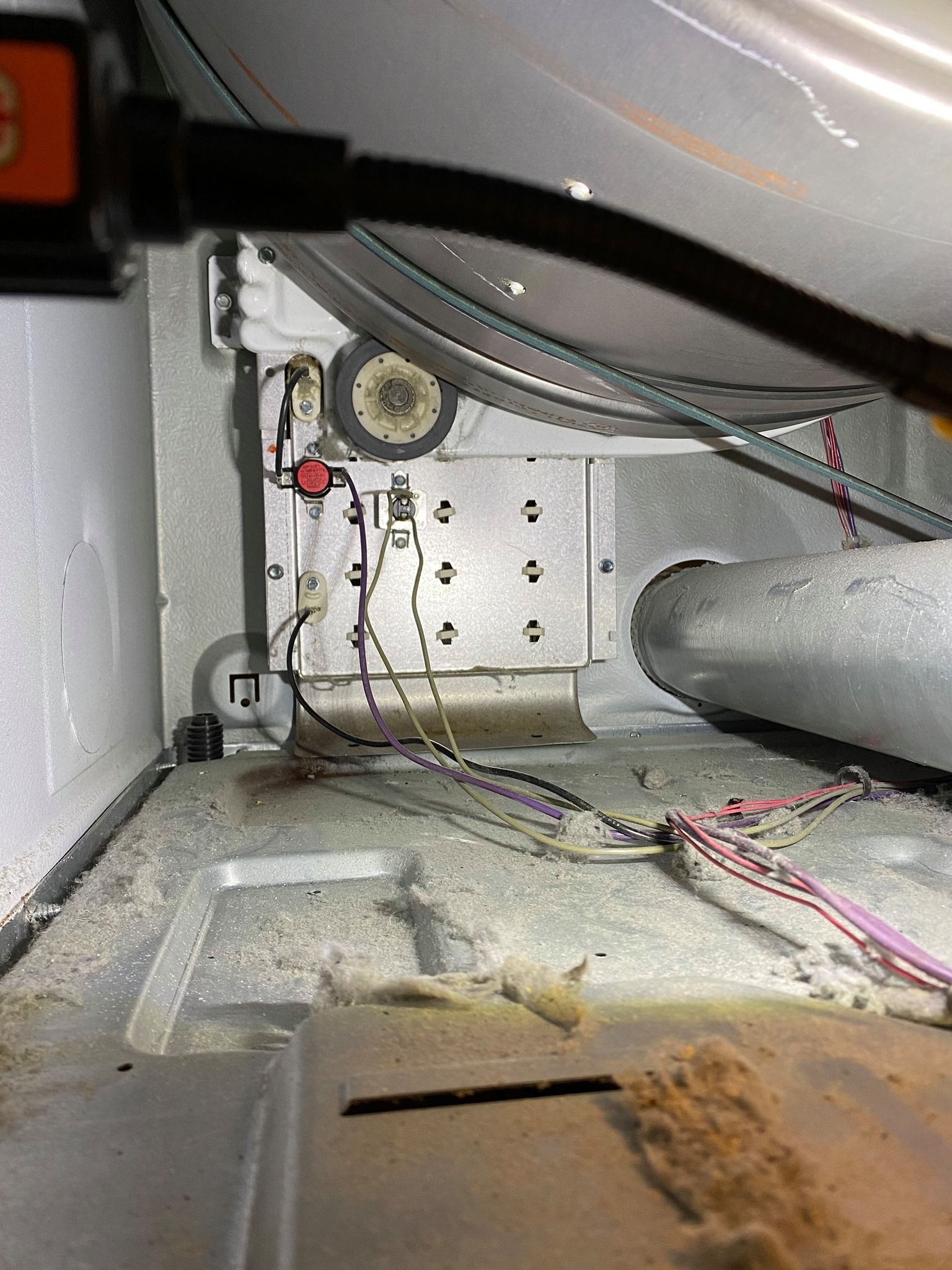 Inside a dryer: heating element, wires, and a metal panel covered in lint.
