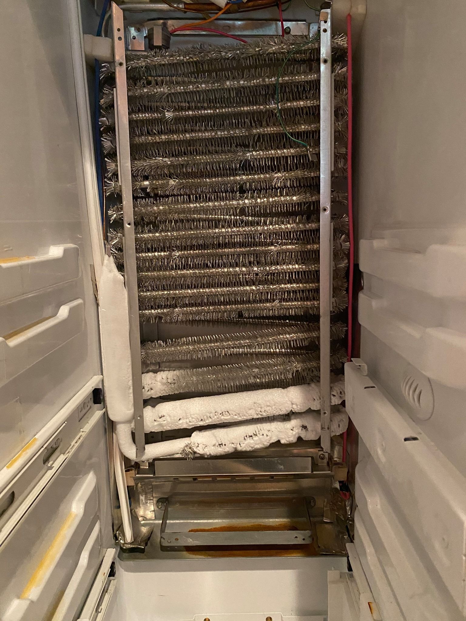 Interior of a freezer with a heavily frosted evaporator coil and shelf, indicating potential defrost issue.