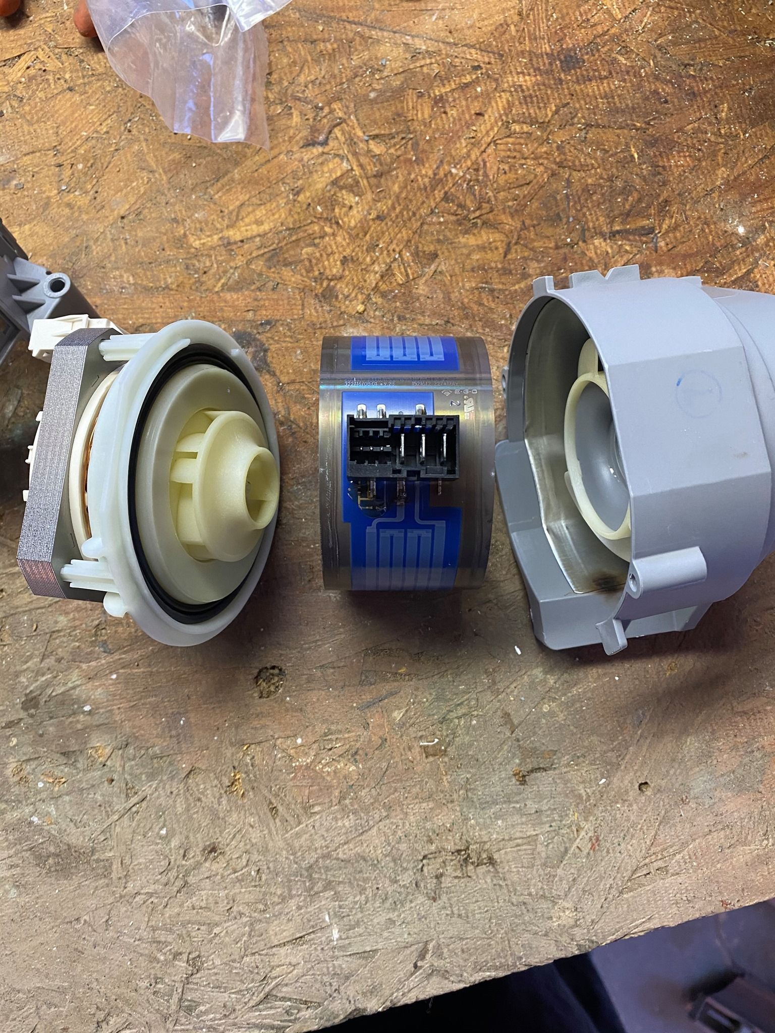 Dishwasher parts disassembled on a wood surface, showing a pump, control module, and housing.