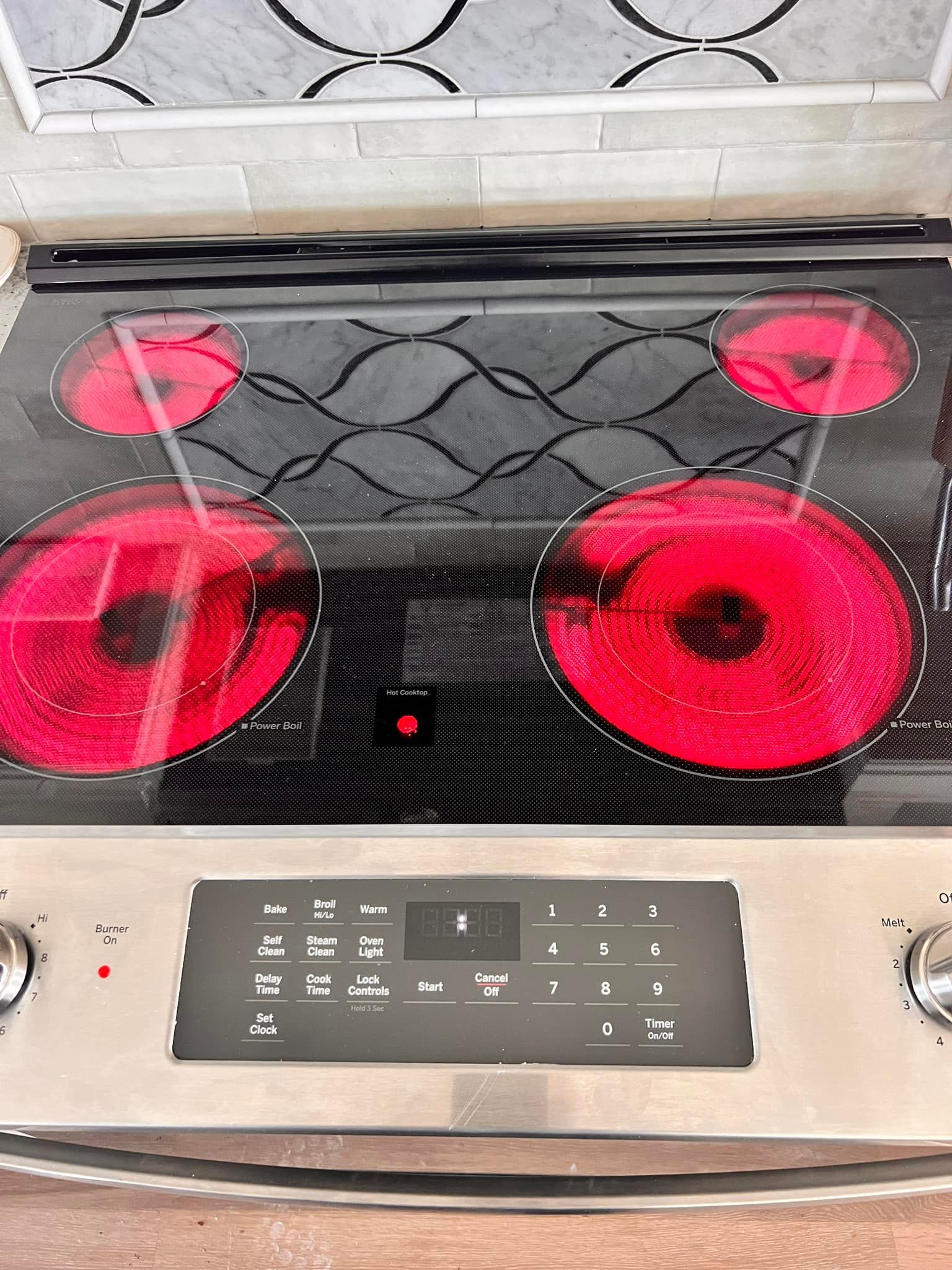 Electric stovetop with four red hot burners, control panel, and patterned black glass.