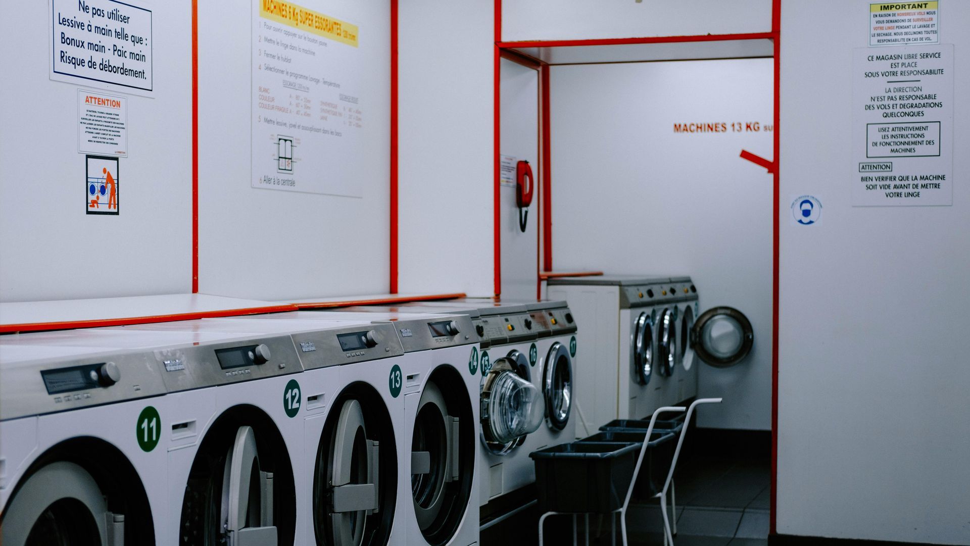 A laundry room with washing machines, laundry carts, and signs on the wall.