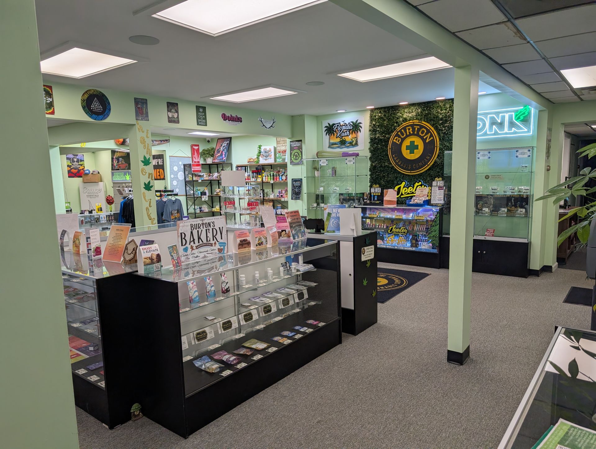 Interior of a cannabis dispensary with products in display cases, bright lights, and green walls.