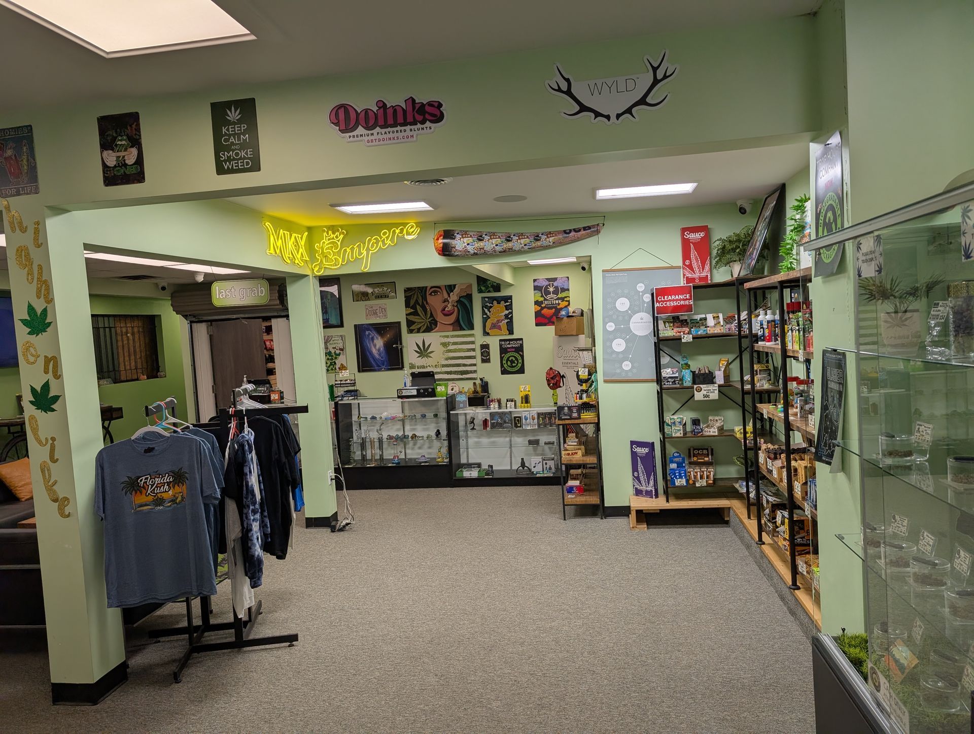 Interior of a retail shop with merchandise and a sales counter. Green walls, clothing rack, and product displays.