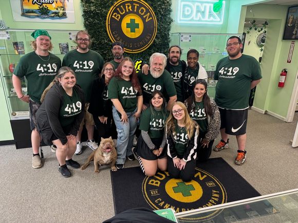 Group of people wearing green shirts posing at Burton Cannabis Company, with a dog on the floor.