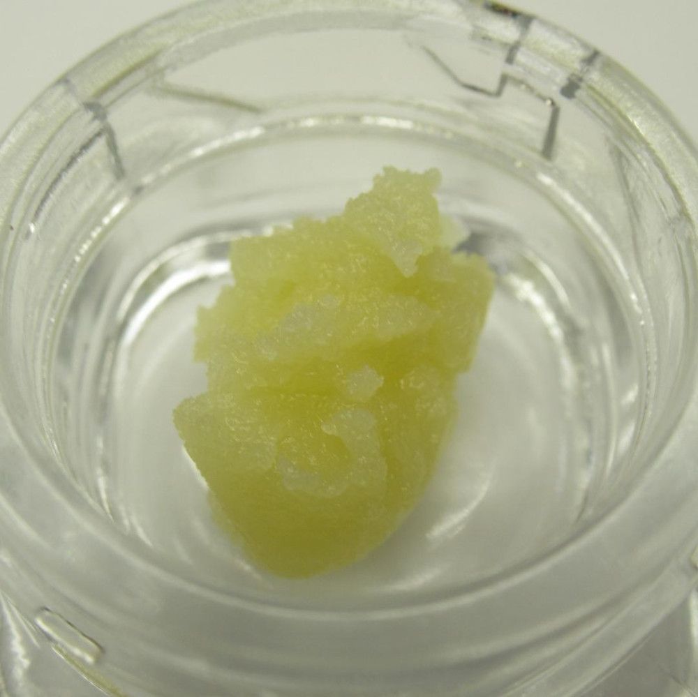 Yellow cannabis concentrate in a clear glass jar, close-up view.