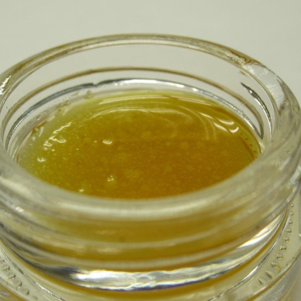 Close-up of a small glass jar filled with yellow-brown, viscous concentrate.