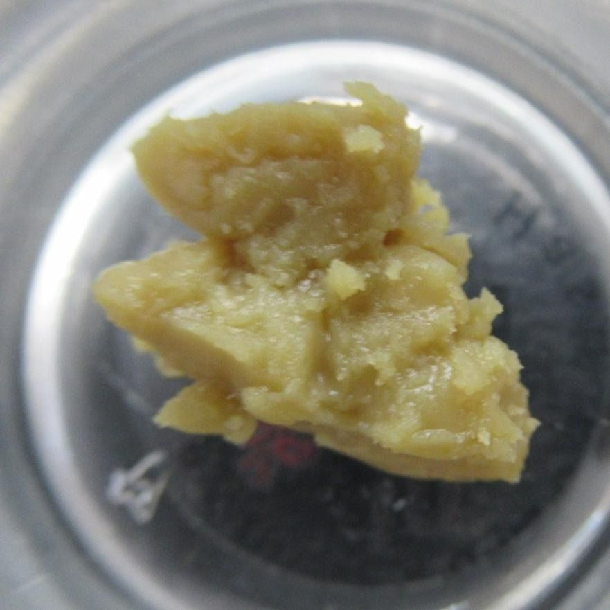 Yellowish, crumbly cannabis concentrate in a glass container.