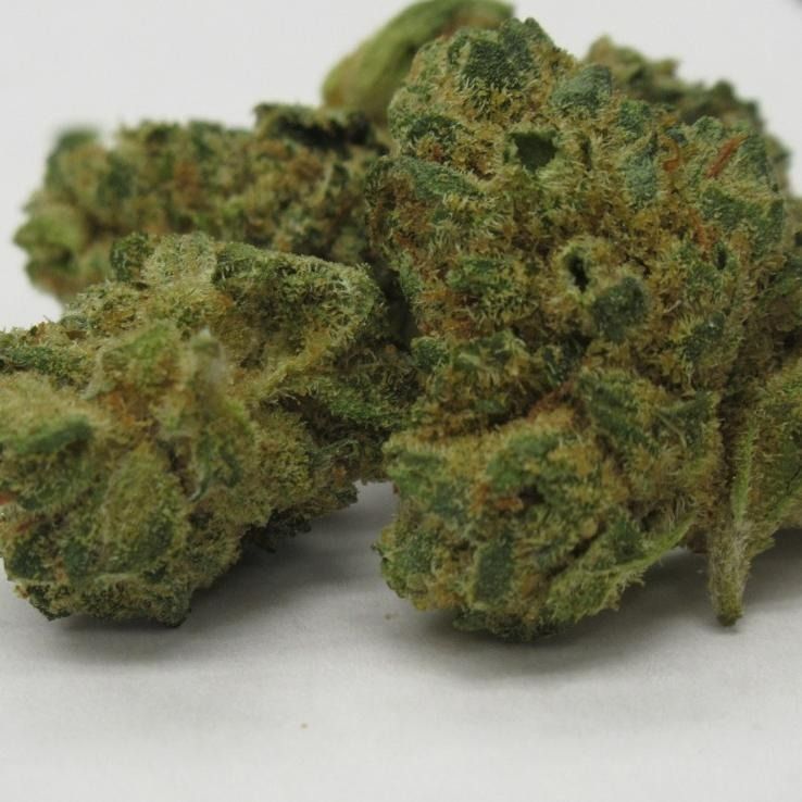 Green cannabis buds with visible trichomes, on a white surface.