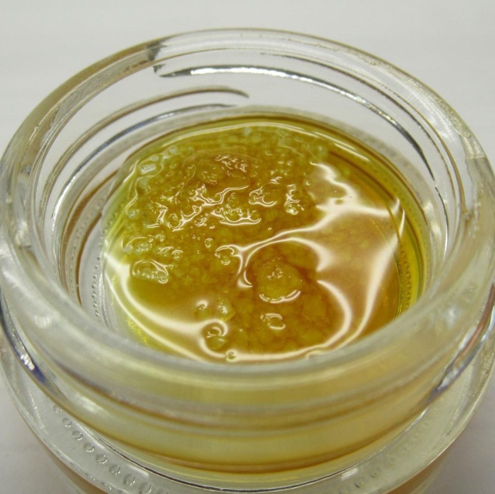 Concentrated cannabis extract in a clear glass jar; a golden, viscous substance with bubbles.