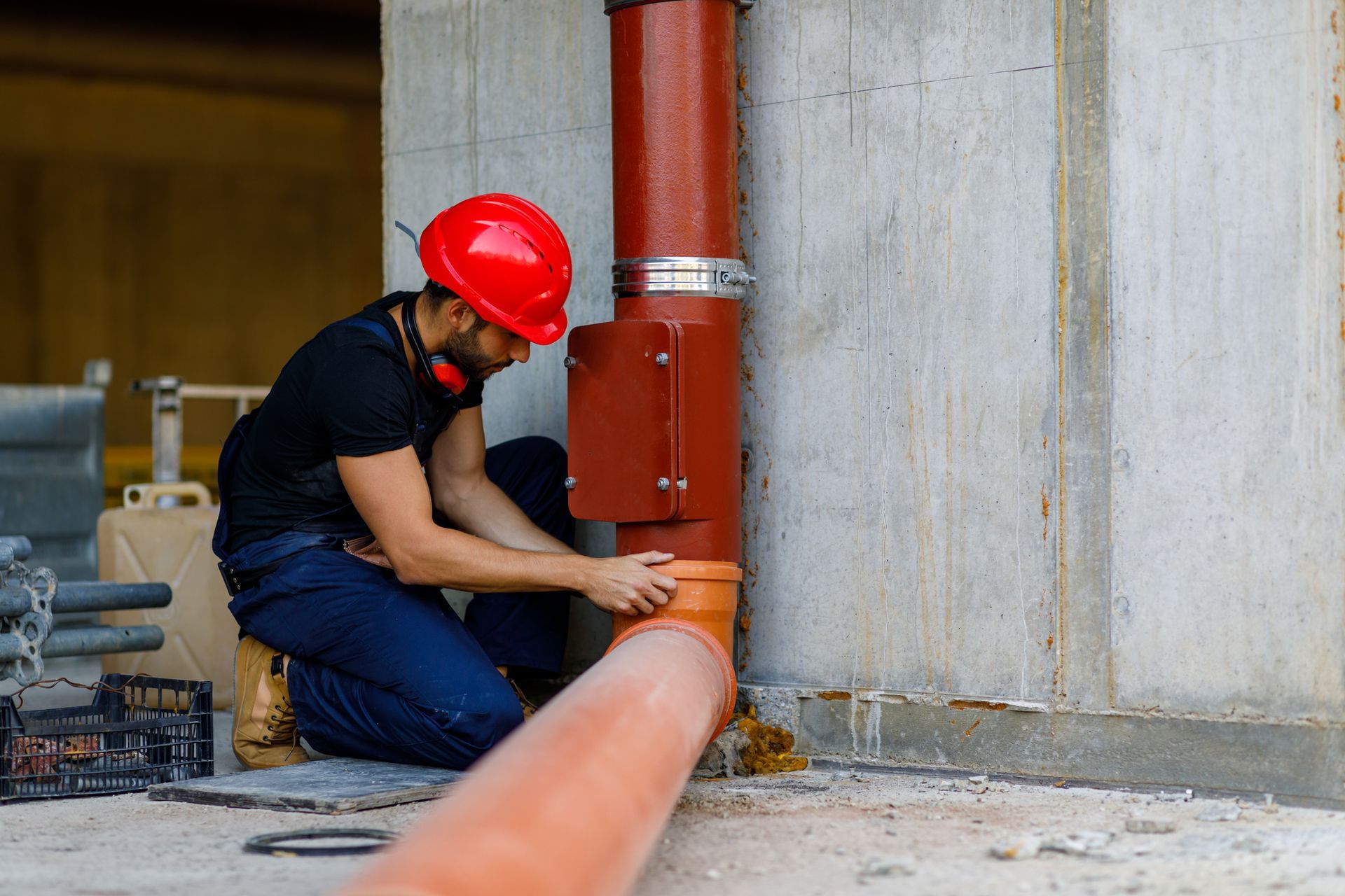 A Man in A Red Hard Hat Is Installing a Pipe on A Construction Site | Neenah, WI | Ogden Plumbing