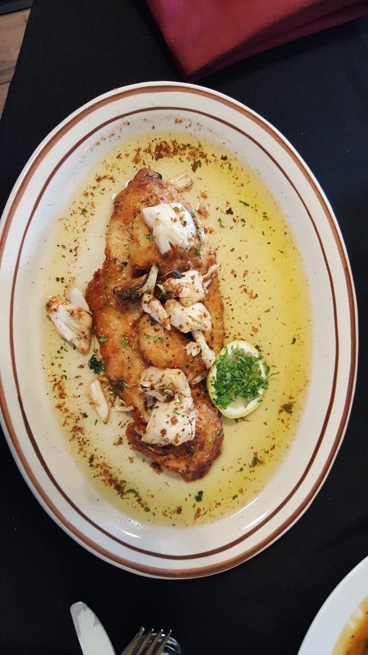 Plate of fish in sauce, topped with crab and a lemon slice.