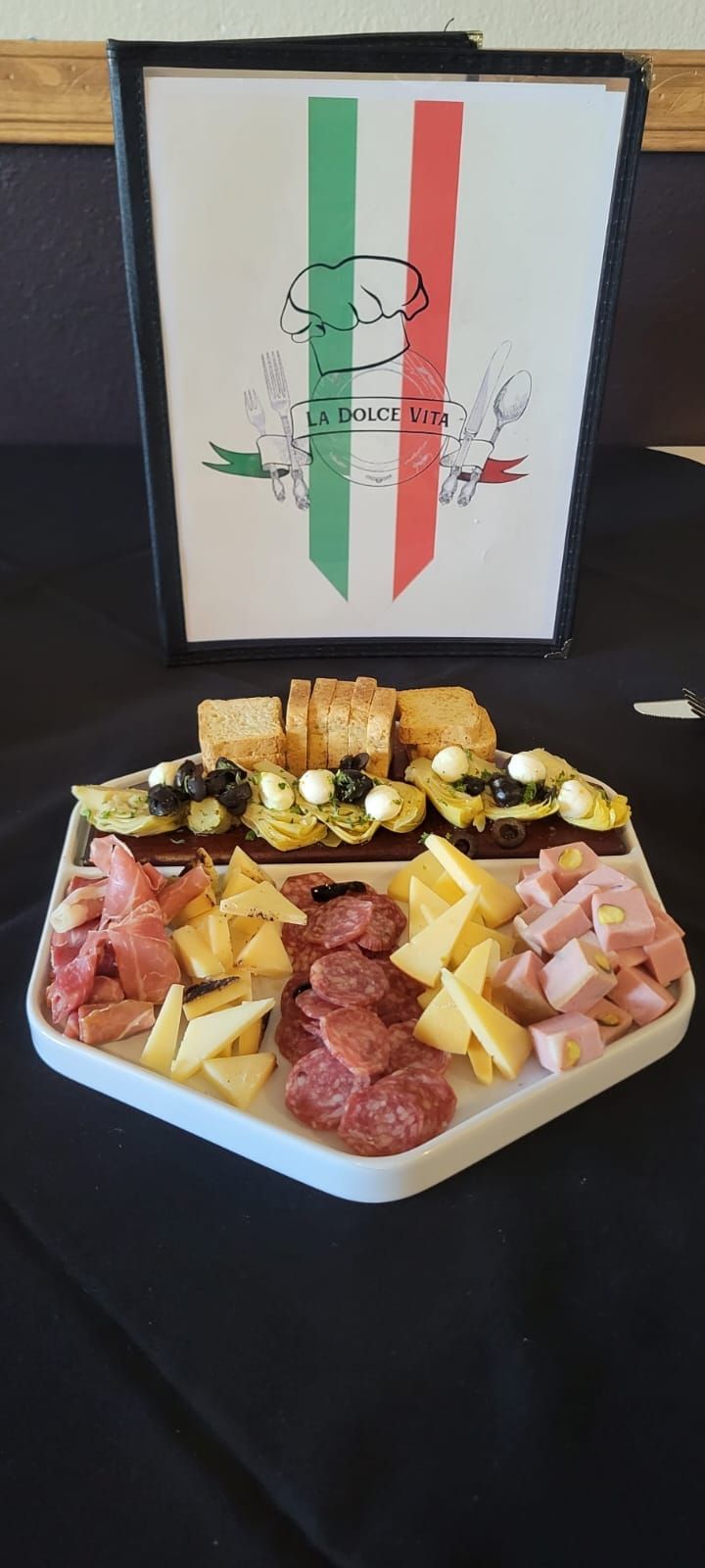 Italian appetizer platter with meats, cheeses, and toasts; under a menu with Italian flag.