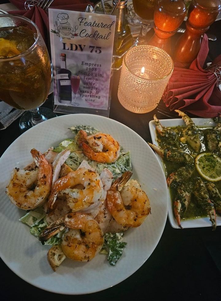 Shrimp salad and crab dish on a table with a lit candle and cocktail.
