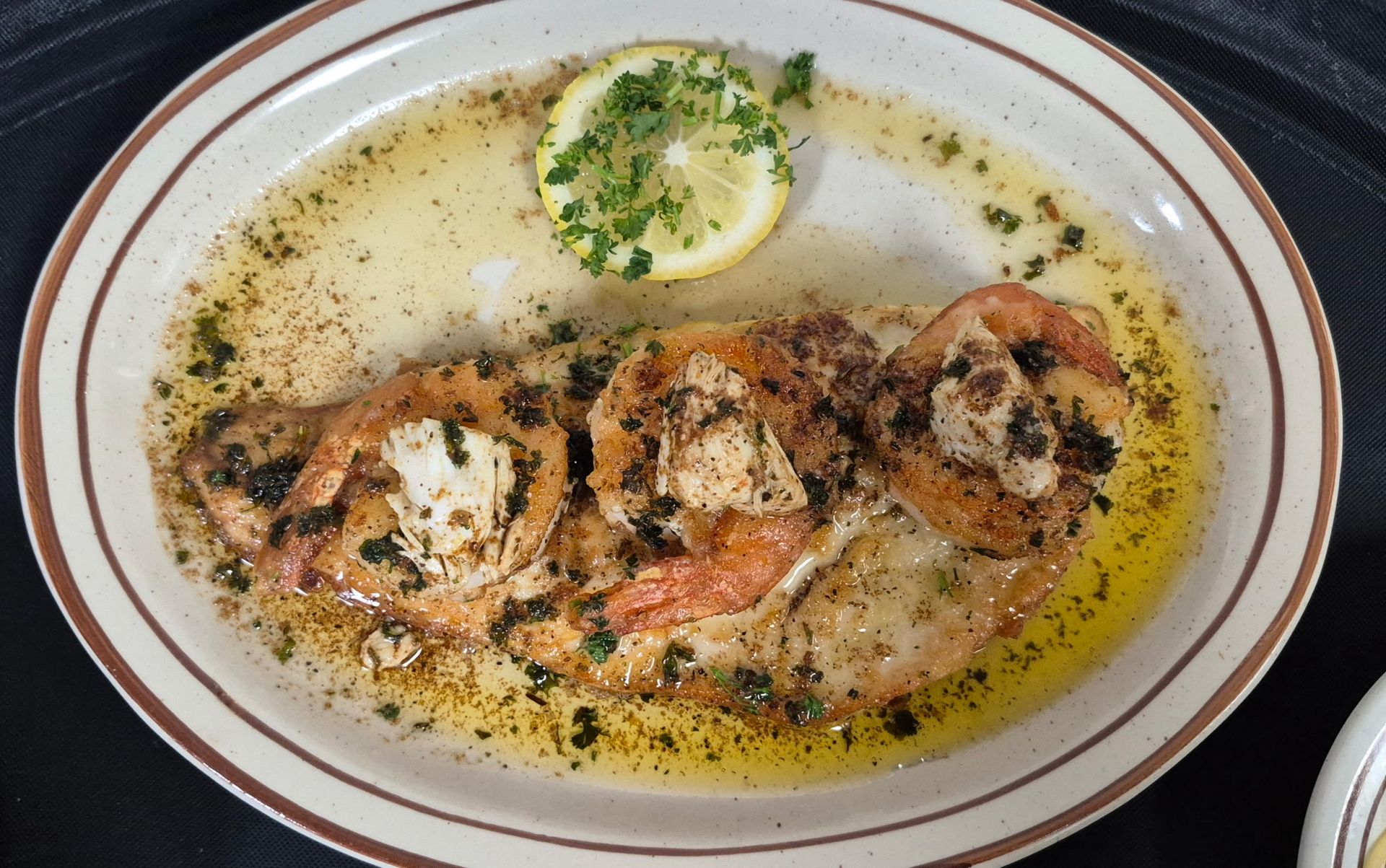 Baked fish with lemon and parsley on a brown-rimmed plate.