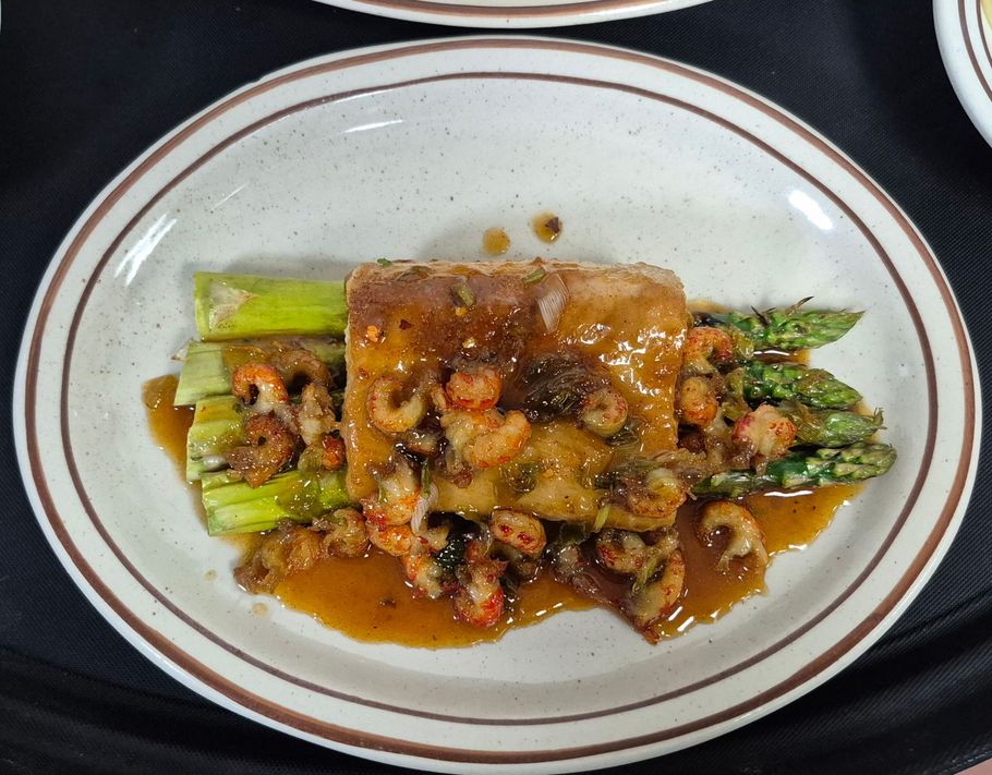 Plate with a square of food, asparagus, crawfish, and sauce. The plate is brown rimmed.