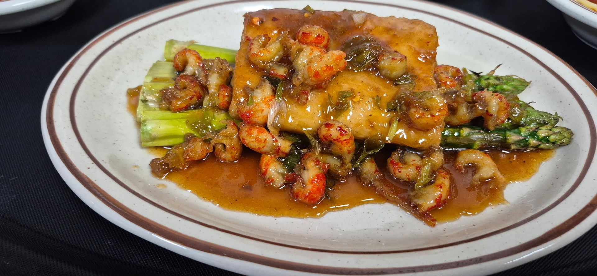 Plate of food with crawfish, asparagus, and sauce.