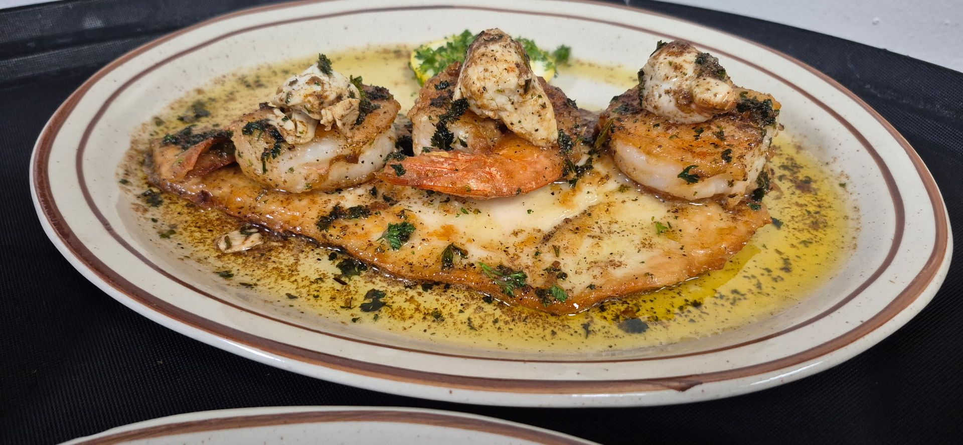 Shrimp scampi served over a bed of fish, drizzled with sauce on a plate.