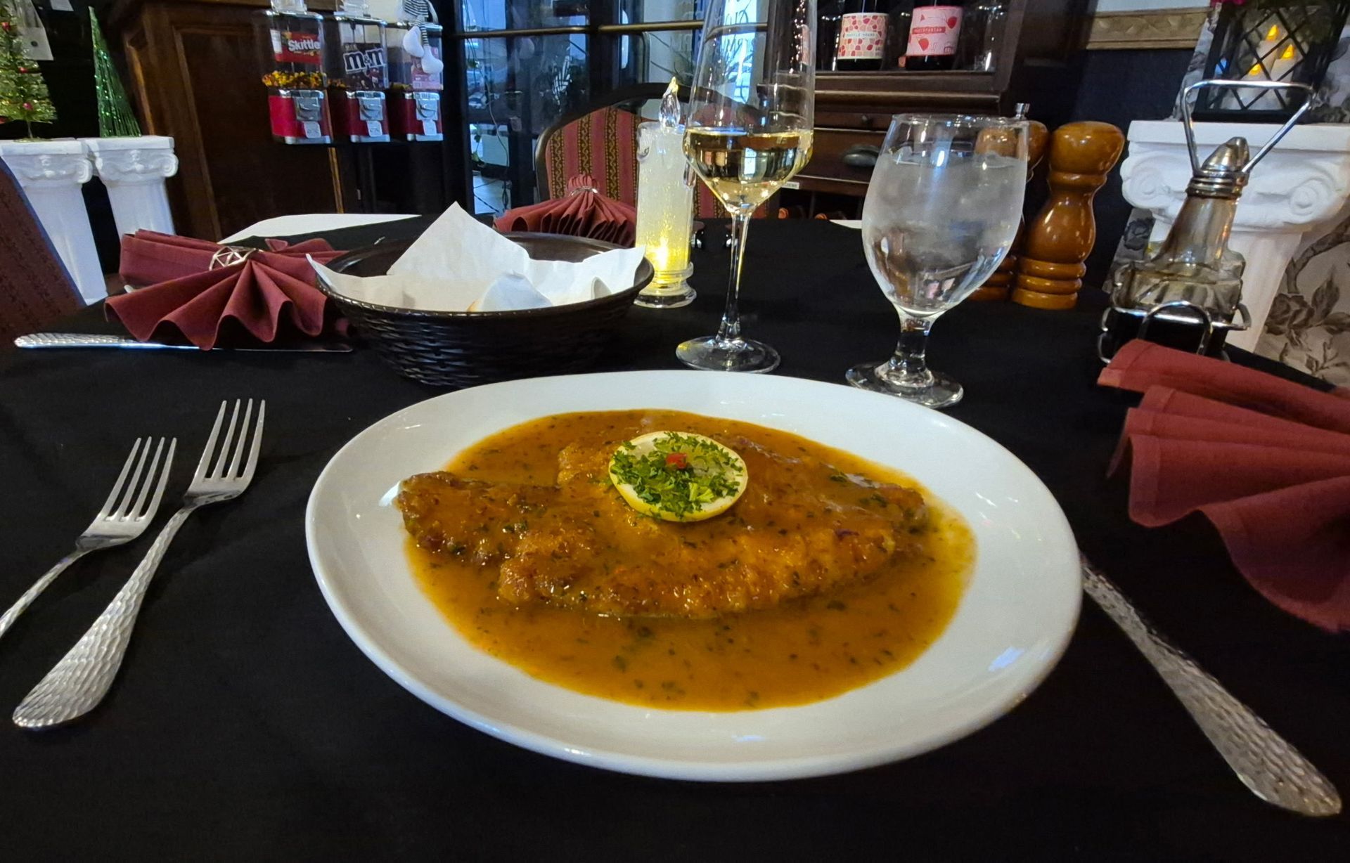 Plate of food in orange sauce with lime garnish on a table set for dining.