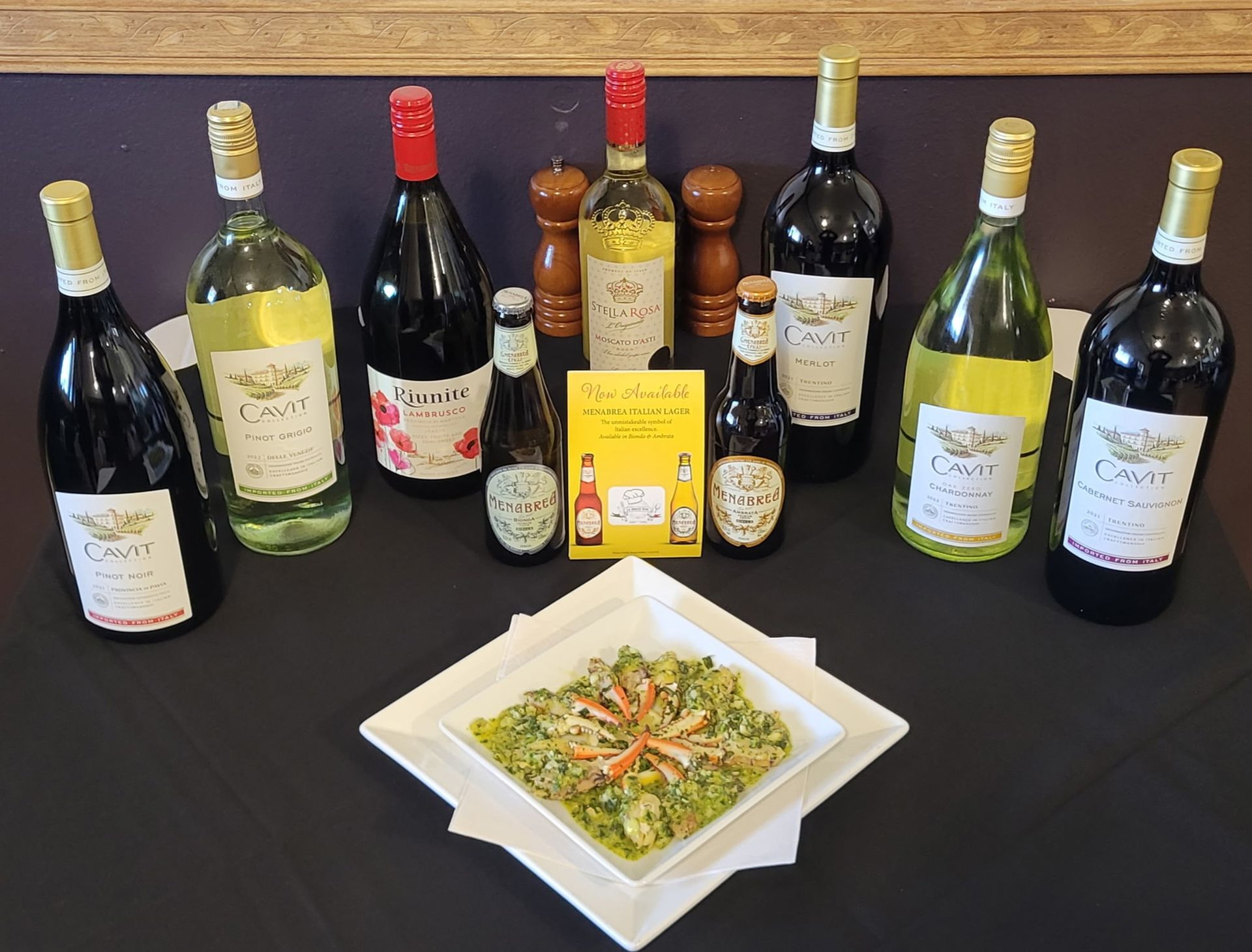Wine bottles and a plate of food on a table. Various bottles surround the dish.