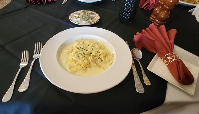 Pasta dish on a white plate with cutlery, napkin, and salt and pepper on a black tablecloth.