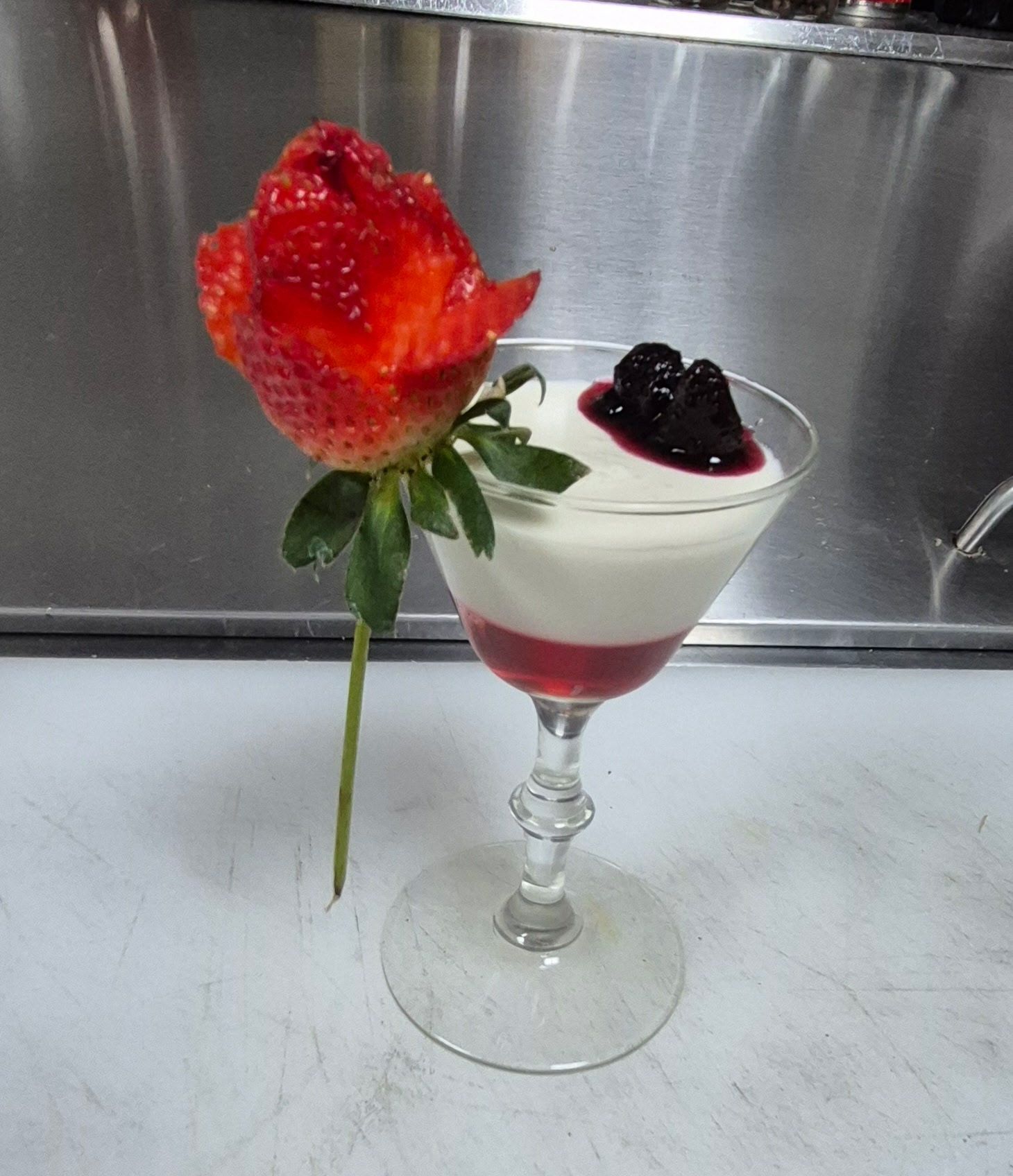 Dessert in a stemmed glass with strawberry rose garnish and berry compote.