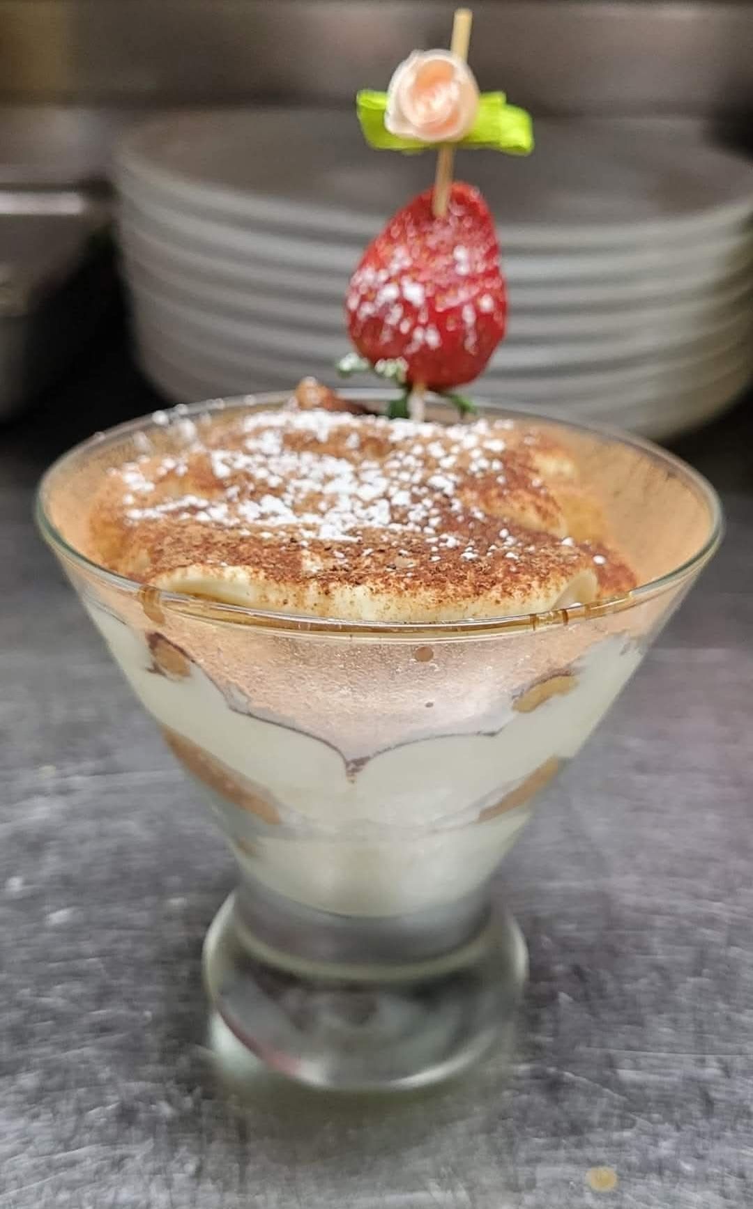Tiramisu dessert in a glass, topped with a strawberry garnish and powdered sugar.
