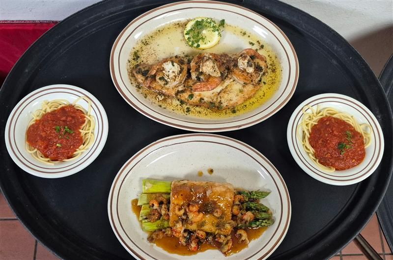 A tray with two plates of seafood, asparagus, and two bowls of spaghetti with red sauce.