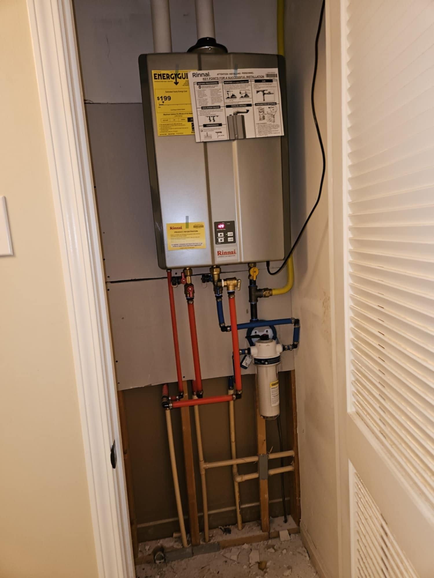 Tankless water heater in a utility closet with red and blue pipes and a water filter.