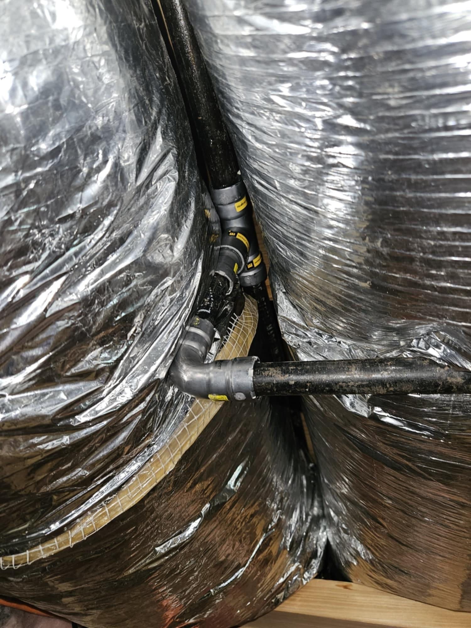 Flexible silver ductwork surrounds a black pipe fitting with several angled connections.