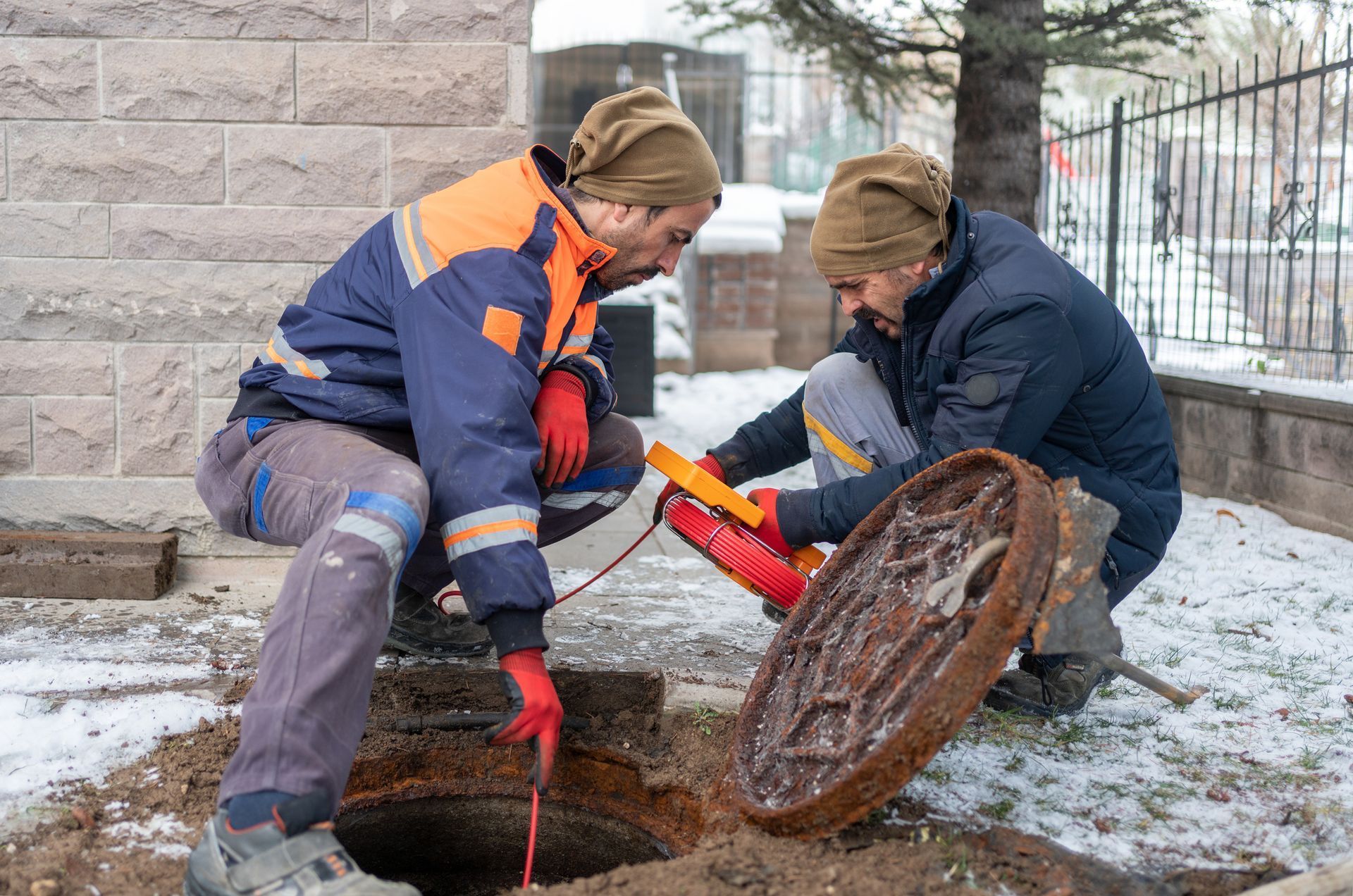 Two workers in winter gear inspecting a manhole with tools outdoors. Two workers in winter gear inspecting a manhole with tools outdoors.