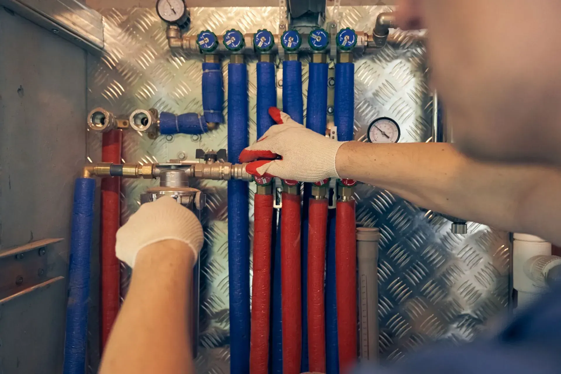 A person wearing gloves adjusts valves on a plumbing system with red and blue pipes.