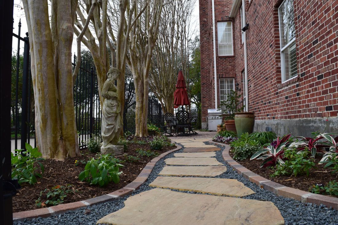 A stone walkway leading to a brick building surrounded by trees and bushes.